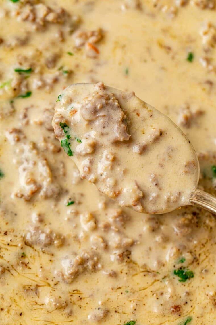 Sausage gravy in a skillet with fresh greens and a spoon.