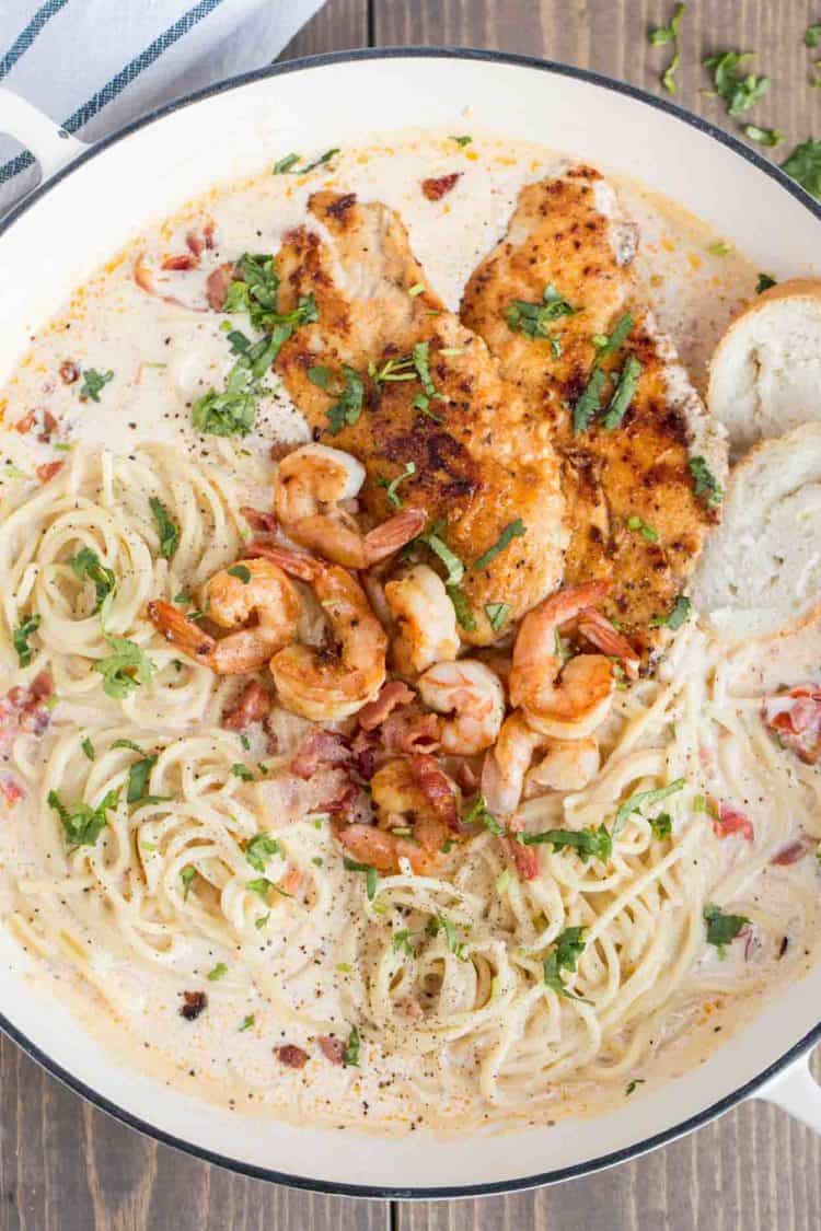Chicken carbonara with shrimp in a skillet with pasta topped with fresh greens.