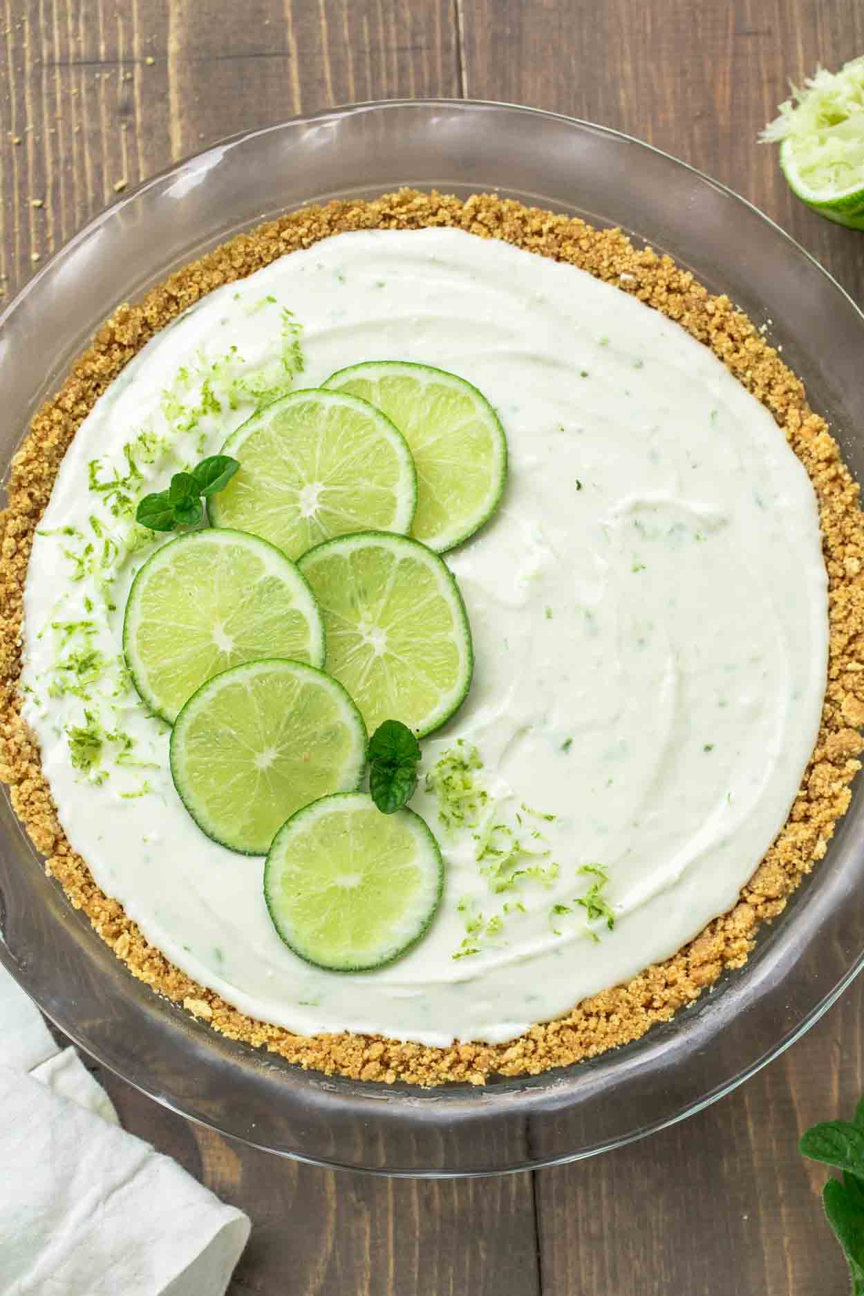 Key lime pie in a pie dish topped with fresh limes and lime zest.