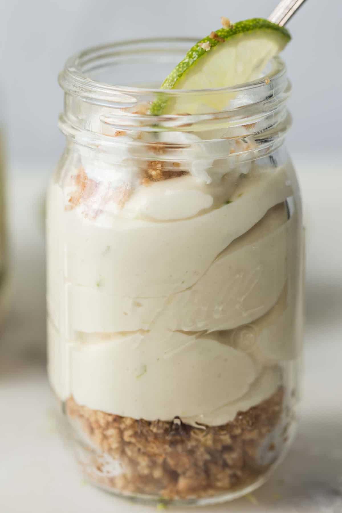 No bake key lime pie in a mini mason jar glass with a spoon and a slice of lime. 