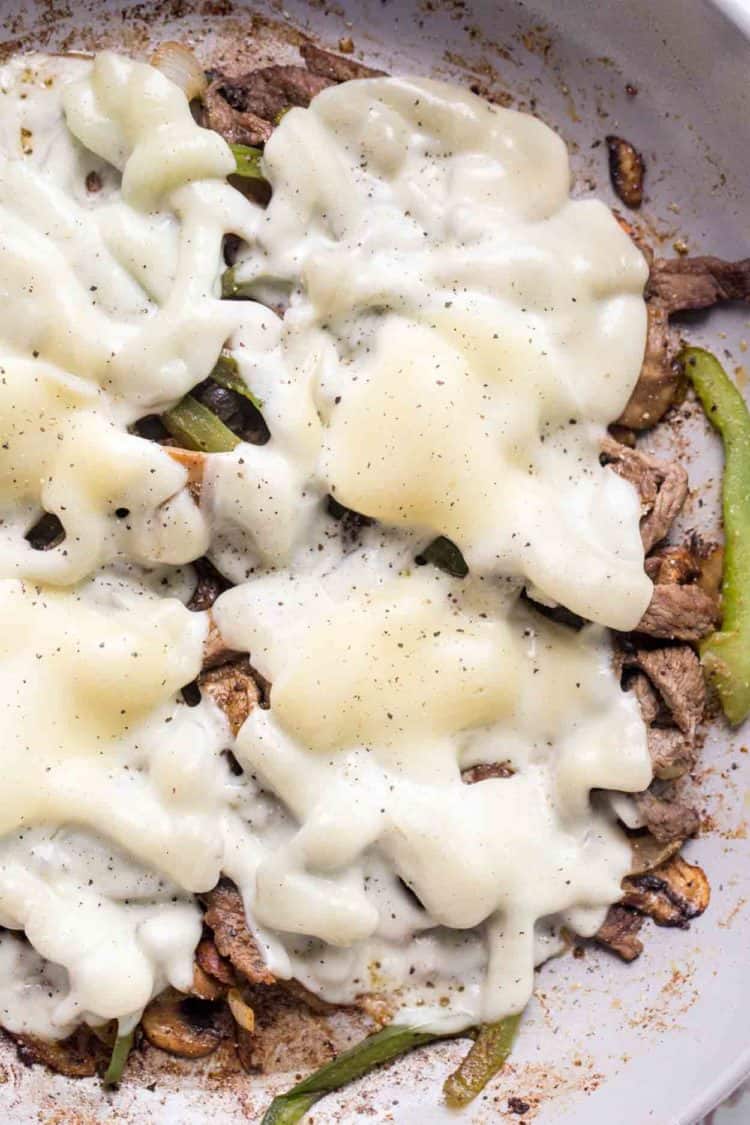 Thinly sliced beef, peppers, mushrooms, and onions topped topped with provolone cheese in a sauteed in a skillet.