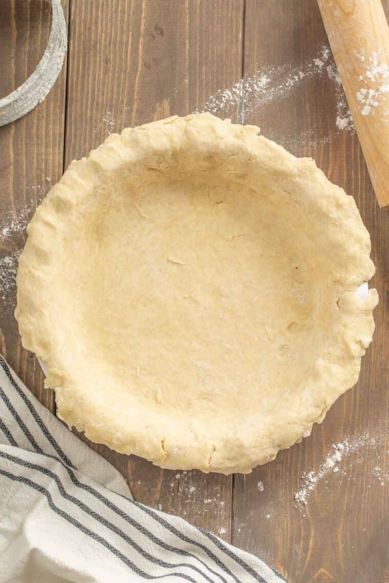 Easy pie crust in a white pie dish next to a rag and a rolling pin.