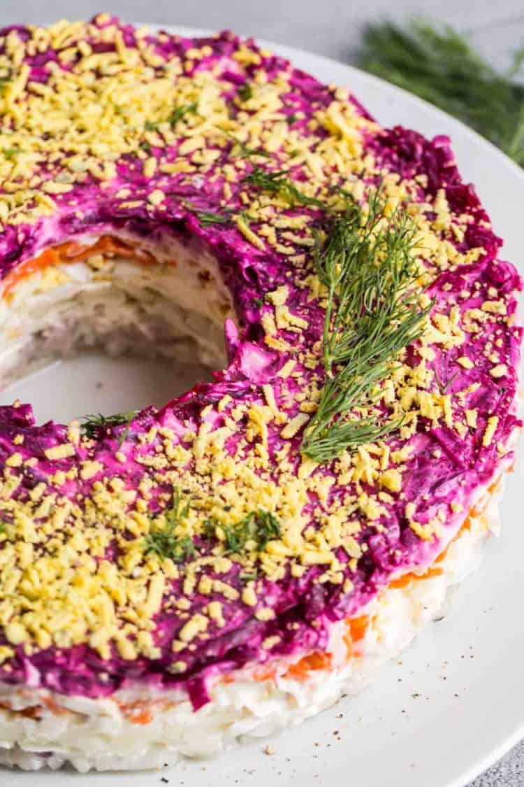 Shuba in a white plate topped with shredded egg yolks and topped with fresh dill.