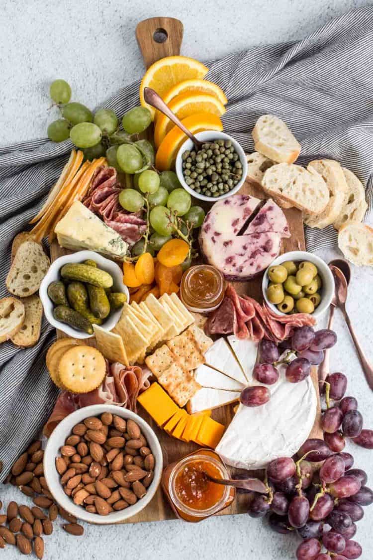A wooden tray loaded with cheese, meats, fruits, nuts and more to make the ultimate cheese board.
