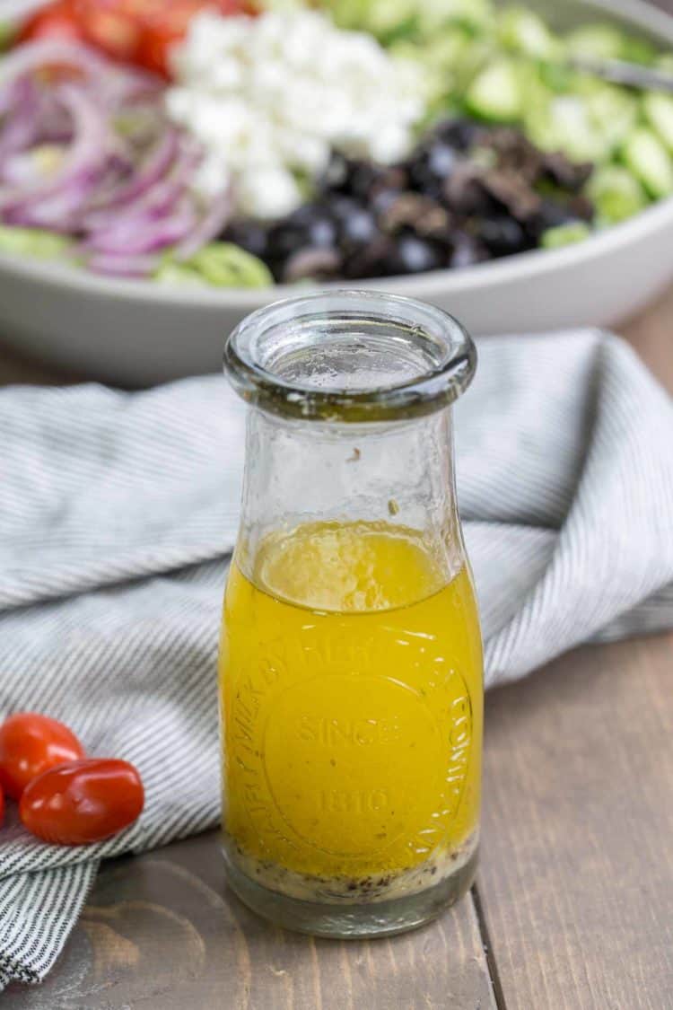 Greek salad dressing in a bottle next to greek salad and tomatoes.