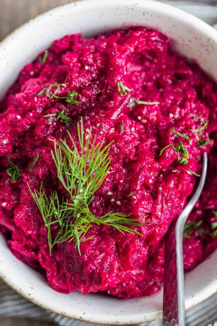 A white bowl of creamy beet horseradish sauce topped with freshly chopped dill. 