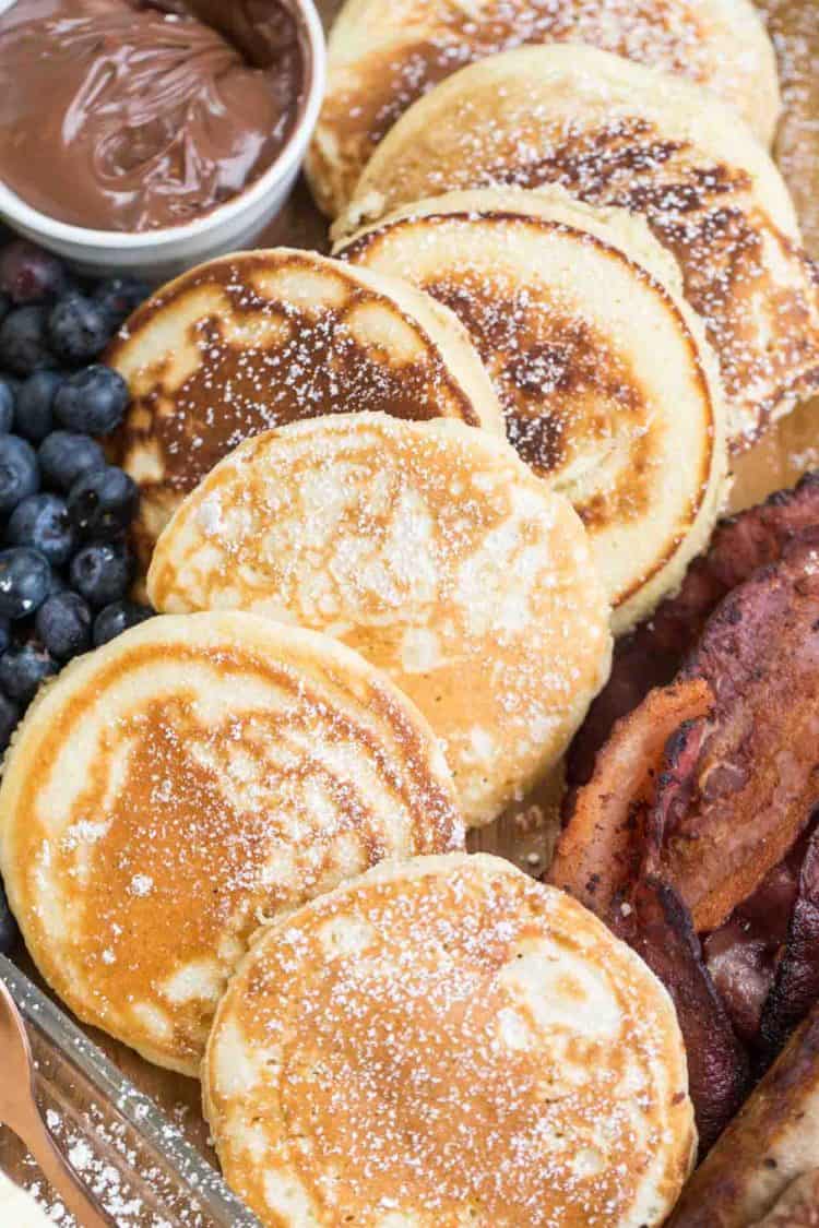 Soft and fluffy pancakes topped with powdered sugar next to blueberries and bacon. 