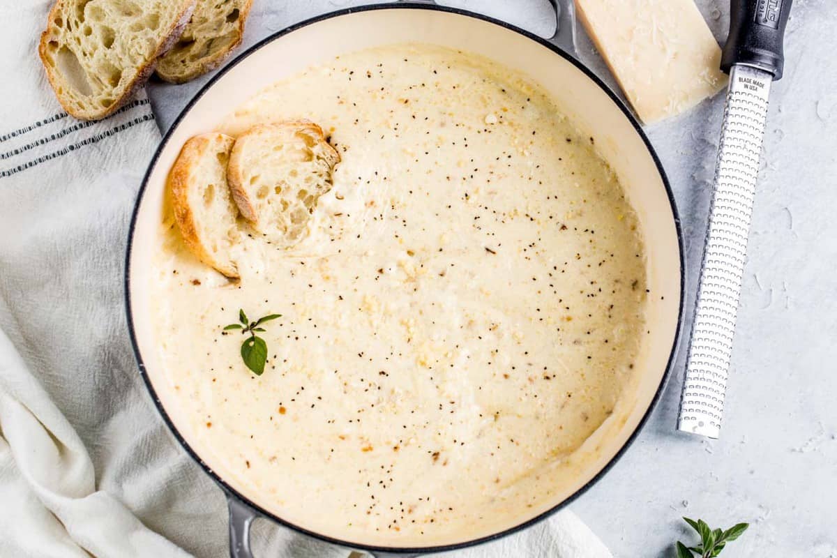 Italian Alfredo sauce in a skillet topped with Parmesan cheese and bread slices.