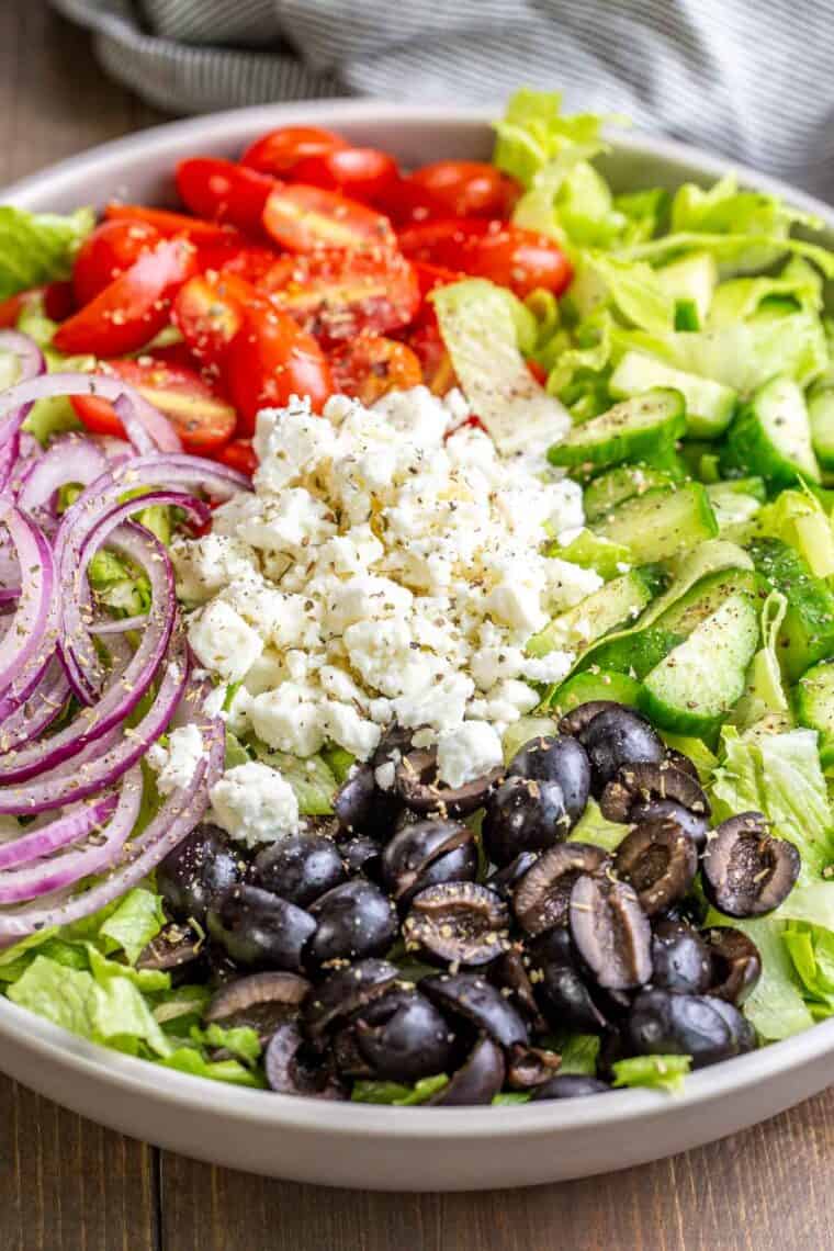 Traditional Greek salad in a gray bowl topped with Italian seasoning. 