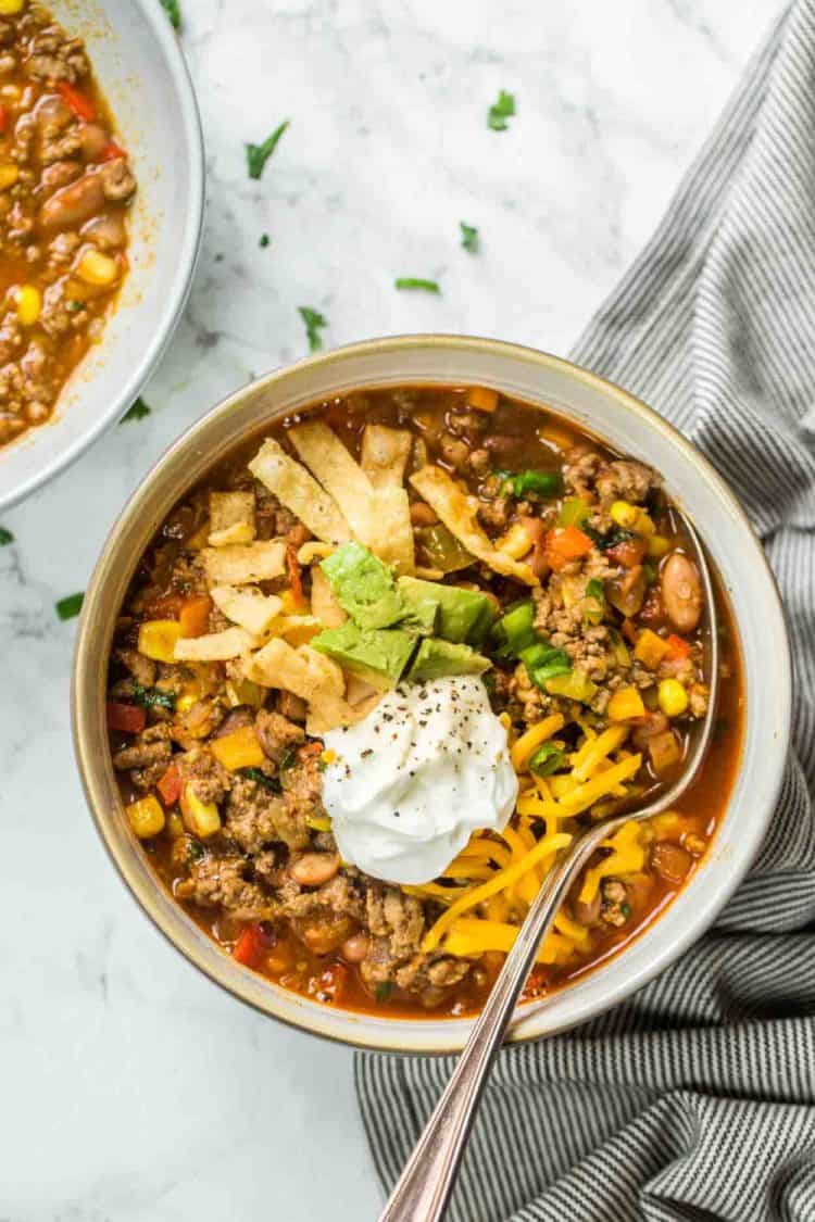 A bowl of taco soup topped with sour cream, cheese, and avocado topped with fresh greens.