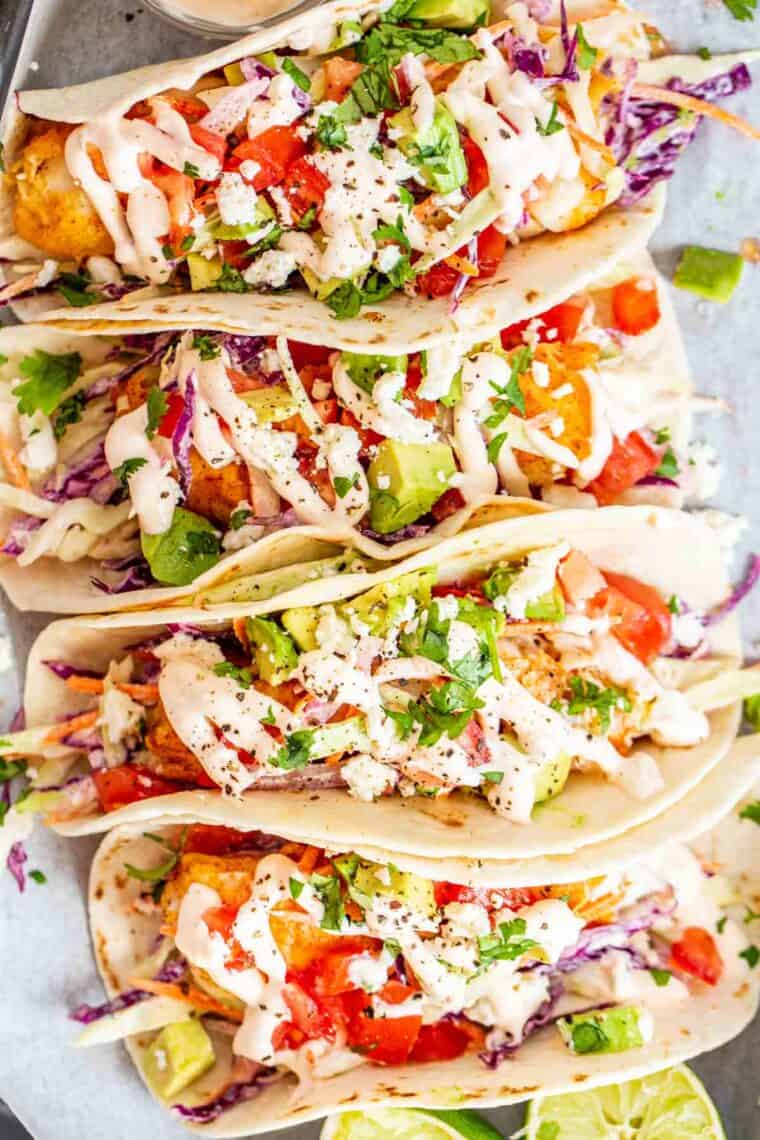 Fish tacos on a plate topped with fish taco slaw, tomatoes and chipotle mayo sauce and fresh avocado.