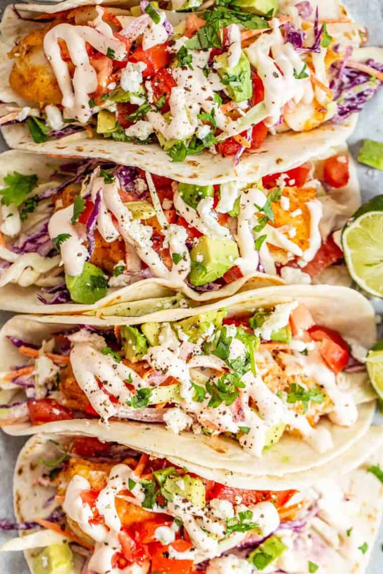 Crispy tilapia fish tacos on a platter topped with toppings and cilantro.