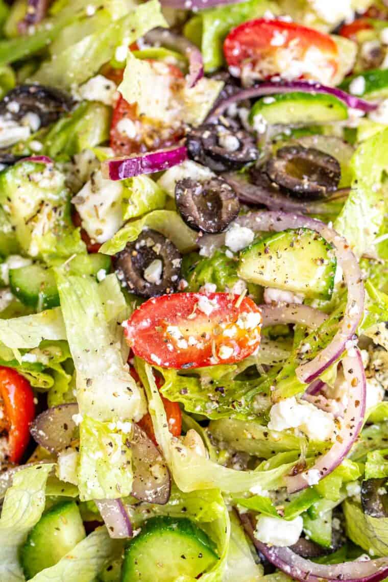 Greek salad tossed in a simple dressing with a spoon and topped with fresh grated black pepper.
