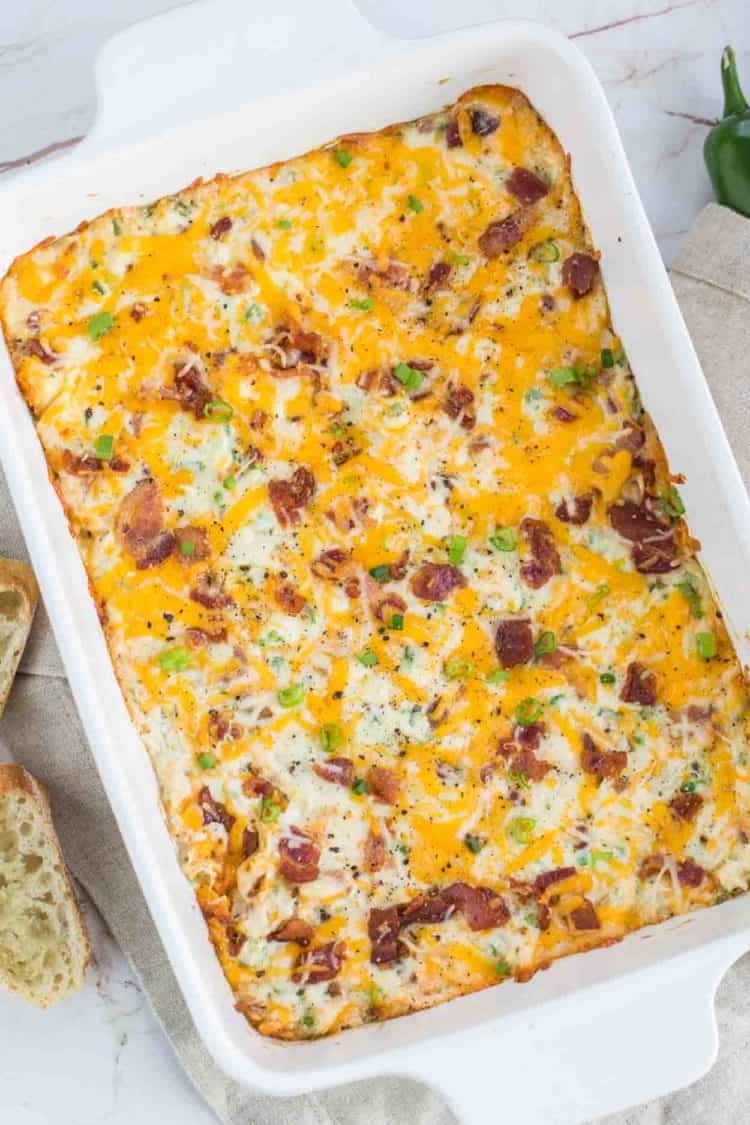 Jalapeno popper dip in a casserole dish topped with bacon, cheese, and chipped greens. 