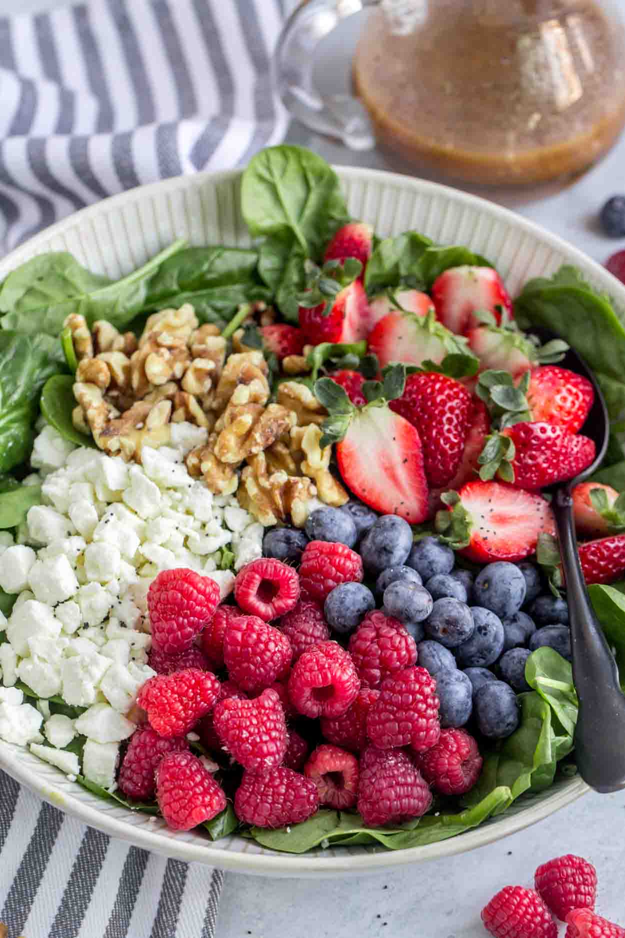 A spinach salad in a bowl with feta cheese, raspberries, blueberries and walnuts. 