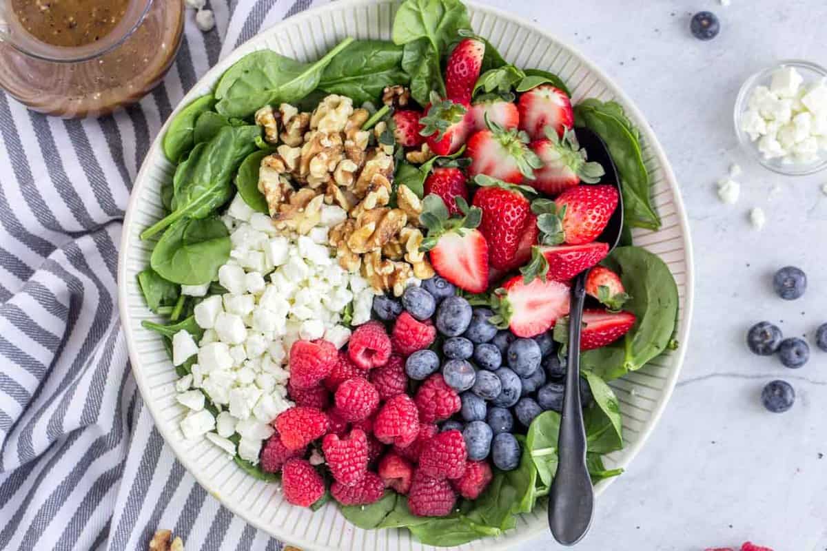 A bowl loaded with spinach, Feta cheese, walnuts and fresh berries. 