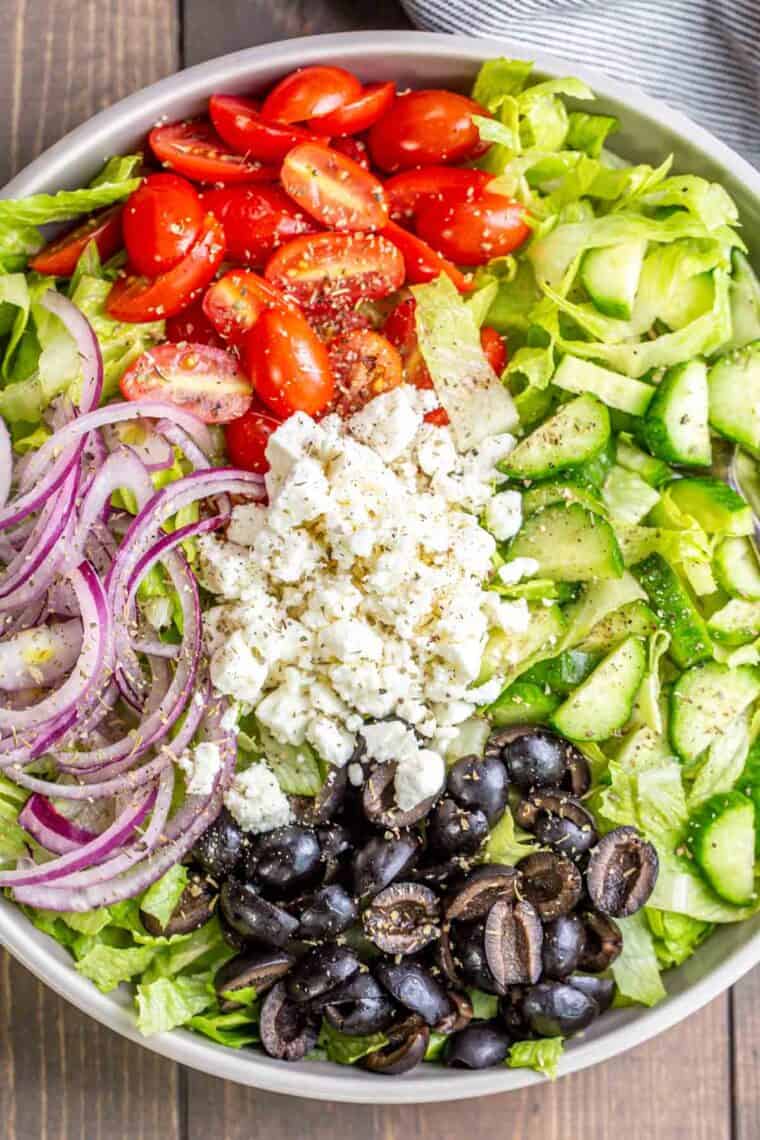 Greek salad in a bowl with lettuce, tomatoes, Feta cheese, and olives.