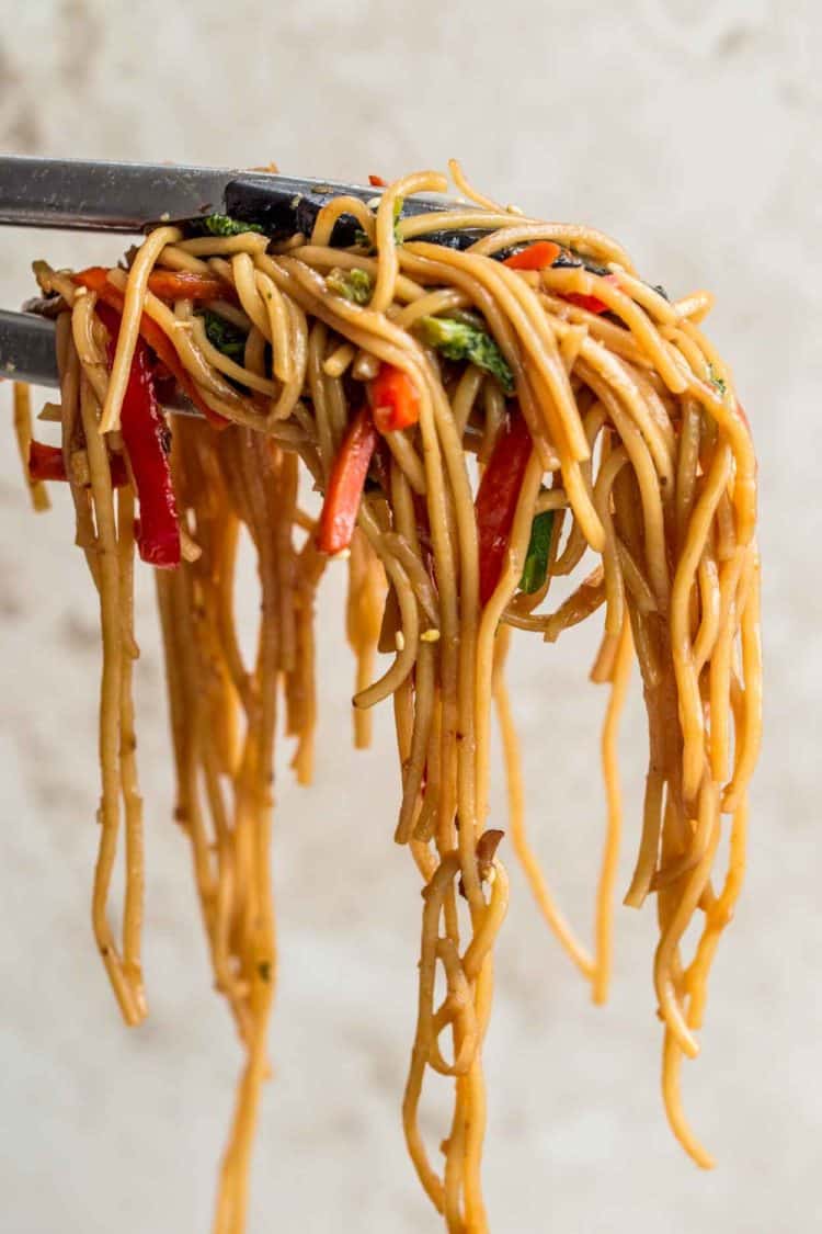 Lo mein noodles with vegetables held up with tongs.