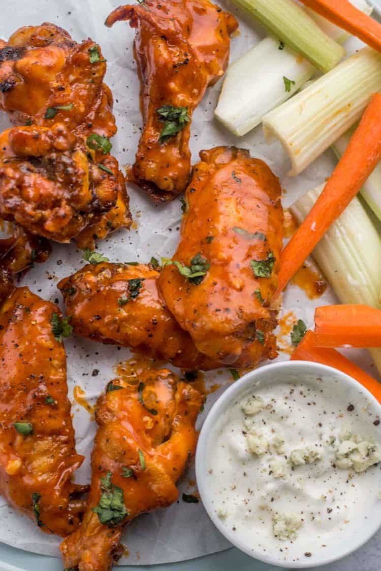 Buffalo chicken wings on parchment paper topped with fresh greens next to a bowl of blue cheese ranch.