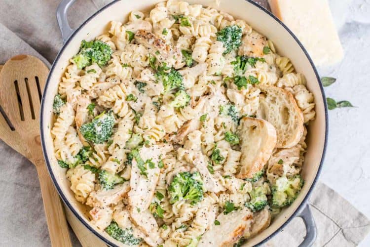 A skillet loaded with chicken Alfredo pasta and broccoli. 