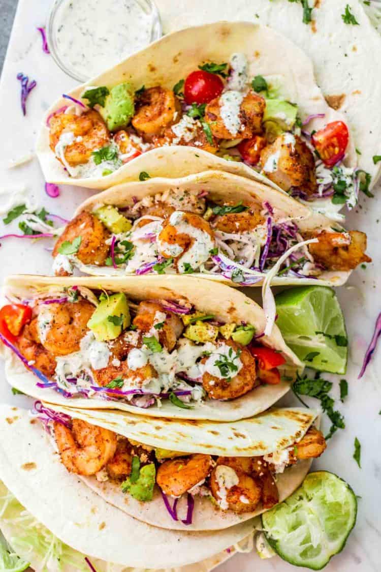 Shrimp tacos on next to each other topped with cilantro lime dressing and Feta cheese.