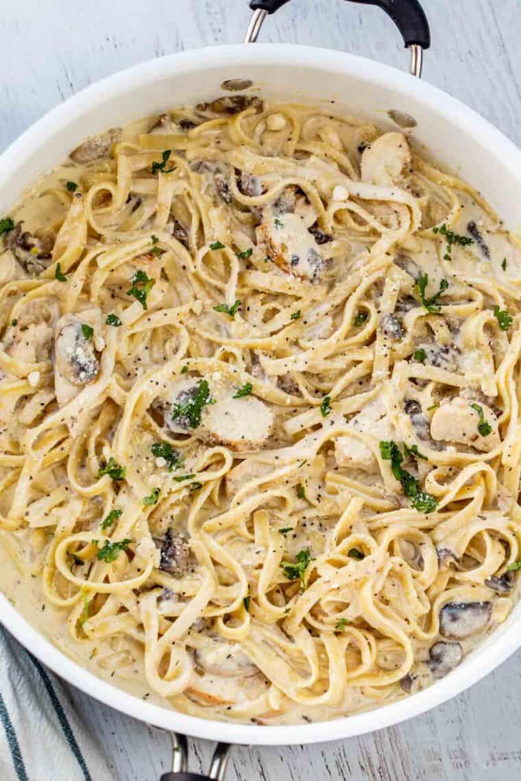 Fettuccine Alfredo in a skillet with chicken and mushrooms, topped with fresh pepper and Parmesan cheese.