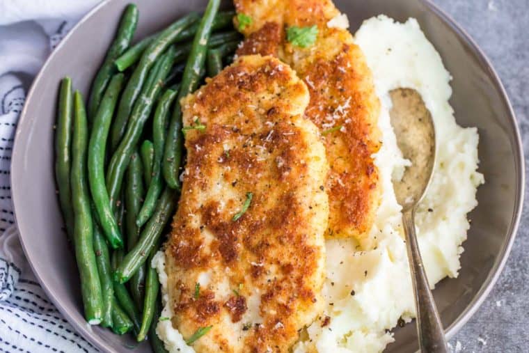 A gray bowl loaded with green beans, mashed potatoes, and parmesan crusted chicken.
