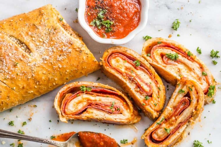 Cheesy Stromboli pizza recipe loaded with marinara sauce and slices topped with fresh greens.