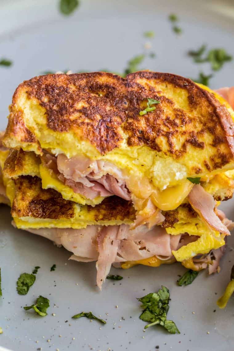 Cheesy breakfast sandwich recipe loaded with ham on plate topped with fresh greens.