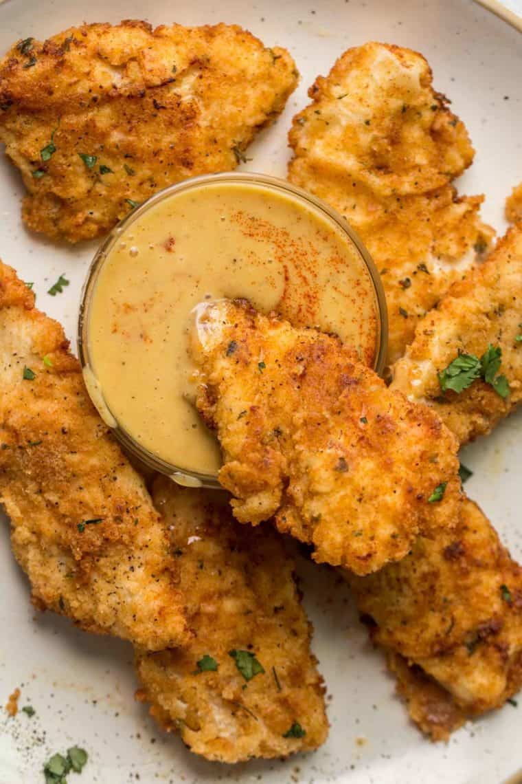Crispy buttermilk chicken tenders in a plate with a small bowl of dipping sauce. 
