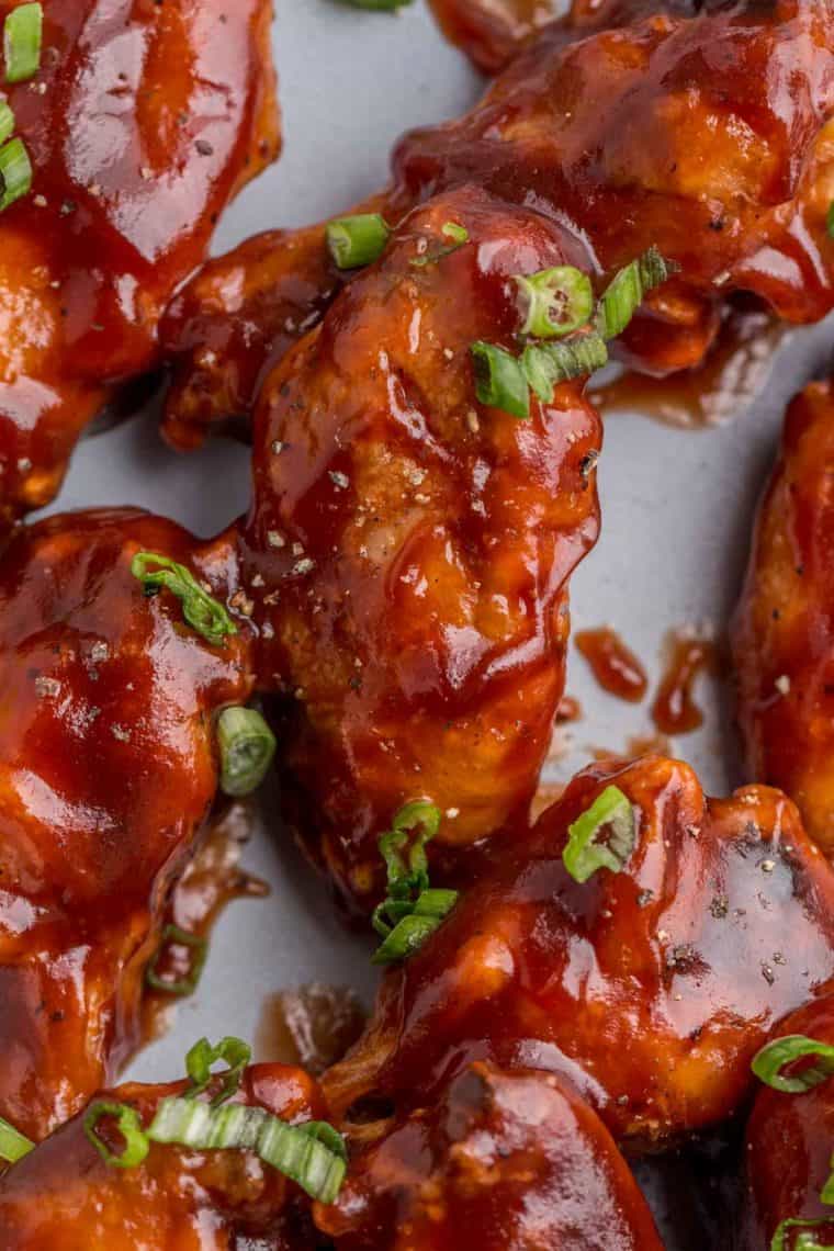 Barbecue chicken wings topped with fresh chopped greens laid out on a blue plate.