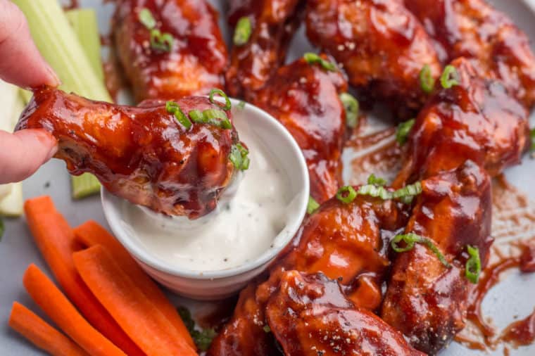 Chicken wings on a plate with one wing being dipped in the ranch in a small plate with celery and carrots on the side.