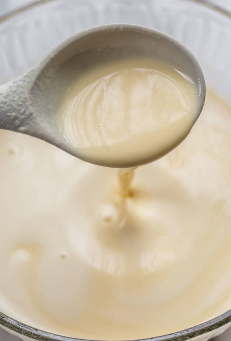 Crepe batter being poured out of a ladle full of crepe batter.