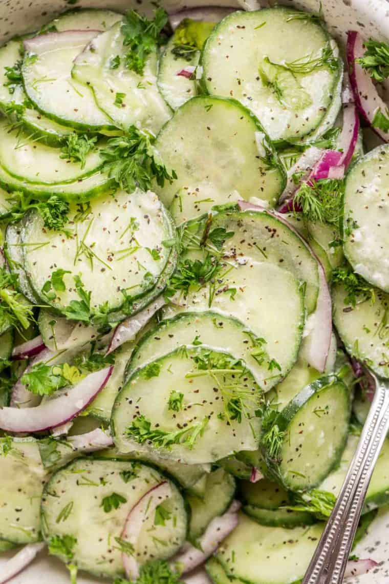 Sliced cucumbers, onion in a bowl topped with dill and black pepper.