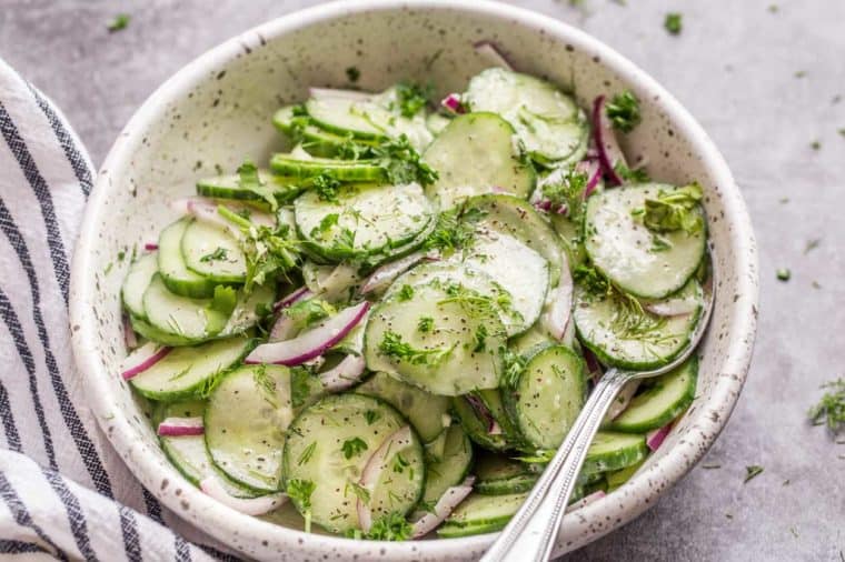 Homemade cucumber salad in a creamy dressing topped with herbs and a napkin on the side.