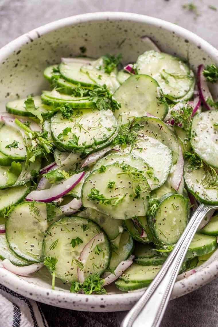 Fresh cucumber salad in a bowl with a spoon and fresh herbs.