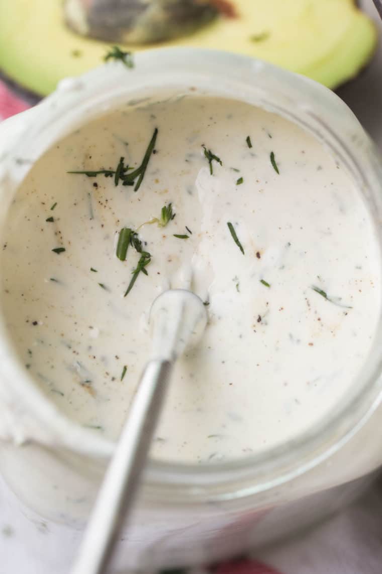Creamy Ranch dressing with a whisk topped with fresh greens.