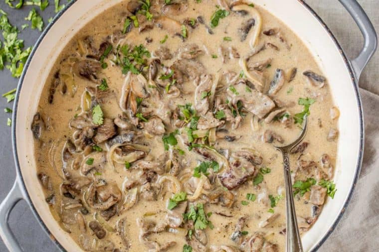Easy beef stroganoff in a white skillet topped with fresh chopped greens.