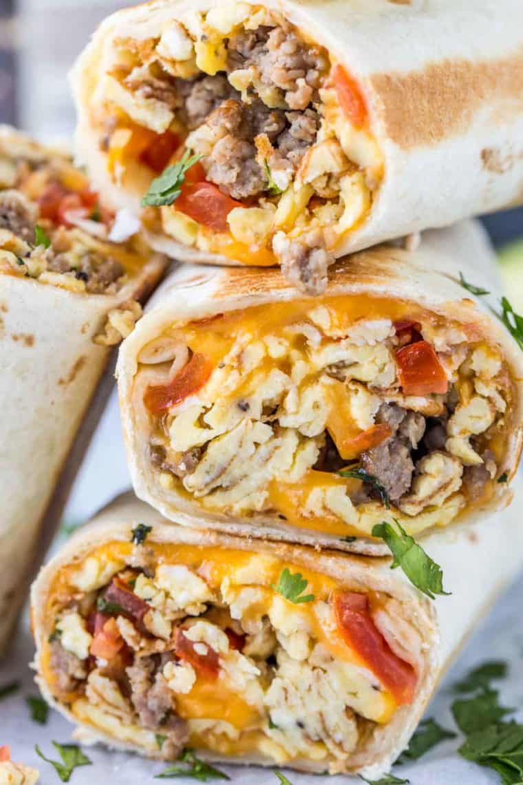 Burritos filled with sausage, eggs and cheese stacked on top of each other topped with fresh greens. 