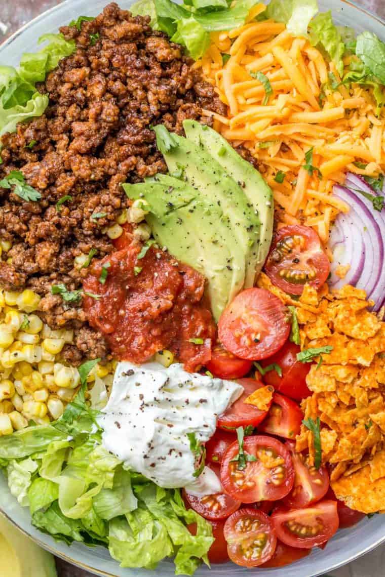 Taco salad in a bowl loaded with ground meat, doritos, salsa, tomatoes and more! 