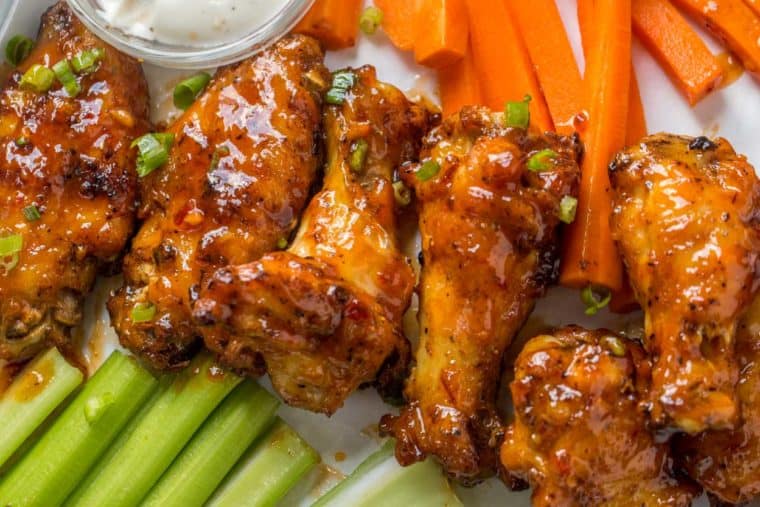 Six Asian chicken wings lined up next to celery and carrots and a bowl of carrots. 