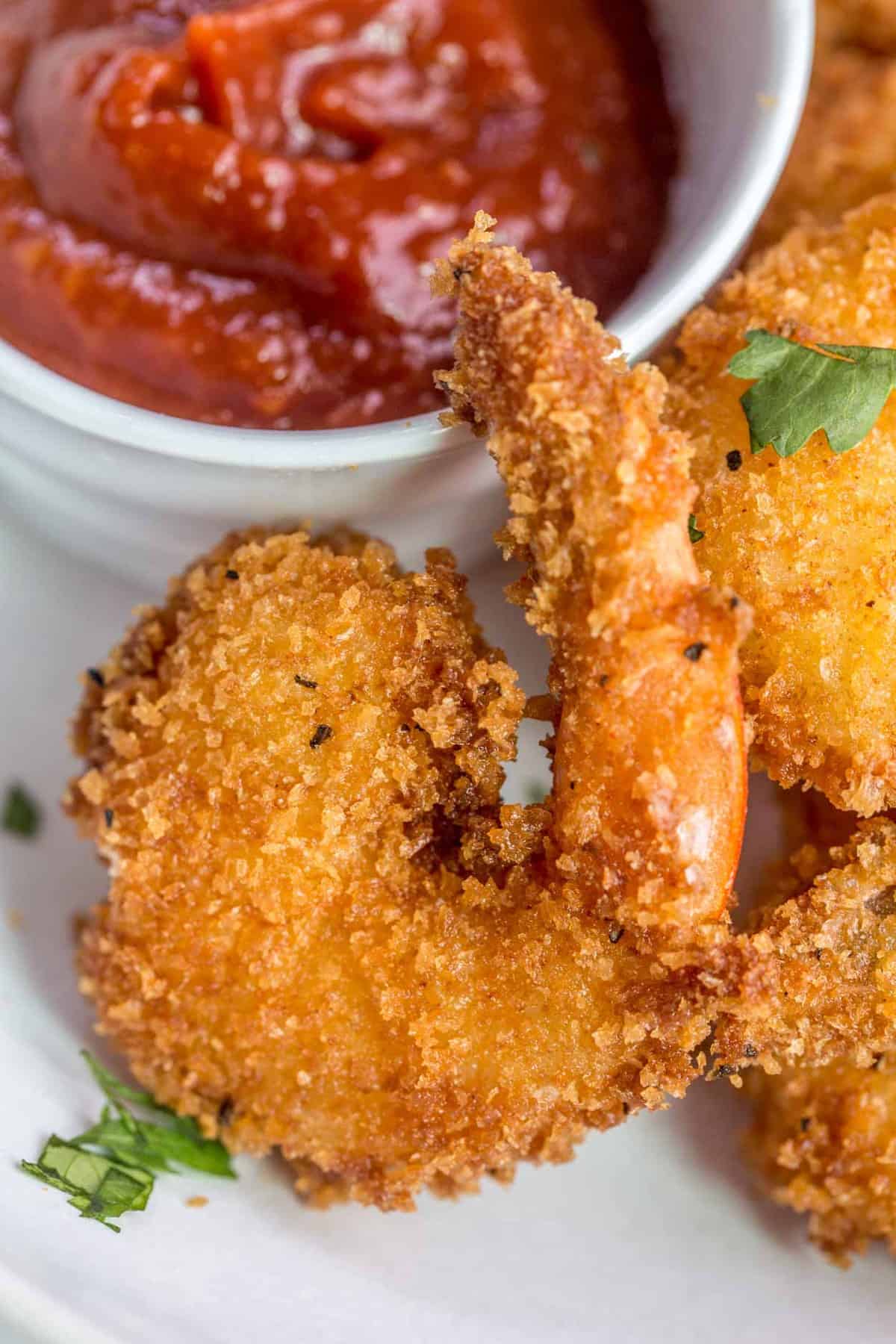A fried shrimp with a bowl of cocktail sauce in the background. 