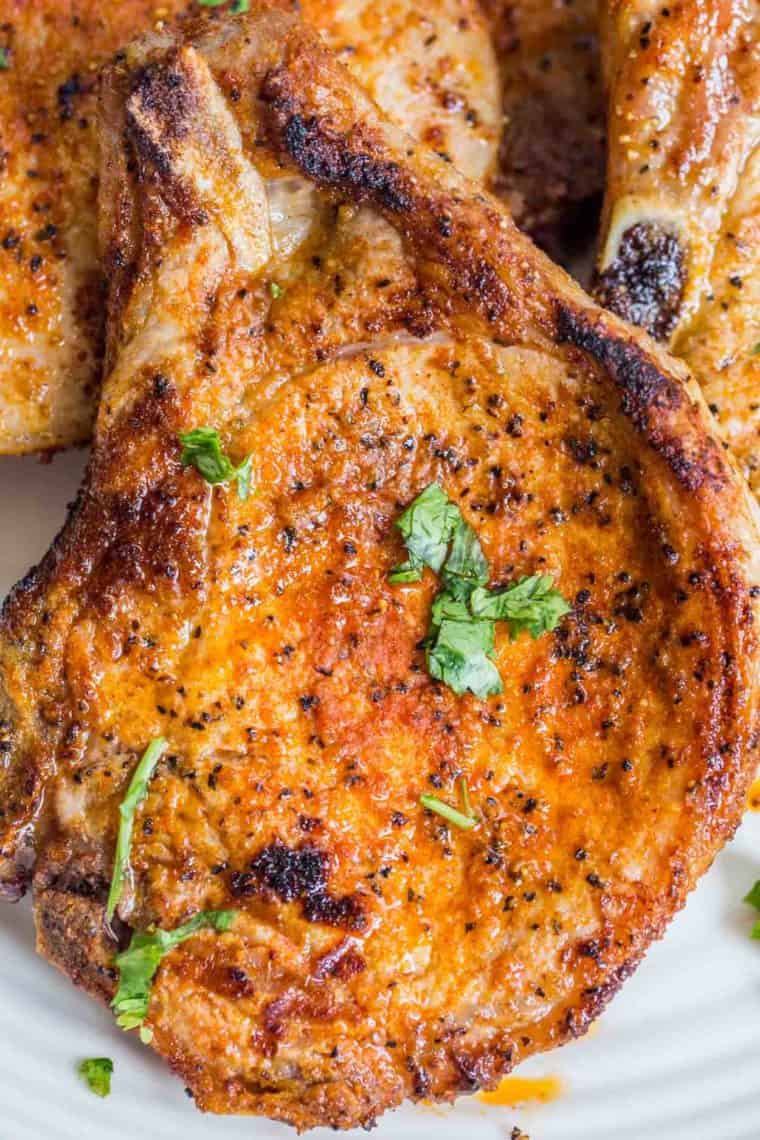 A juicy and tender grilled pork chop on a white plate loaded with fresh chopped greens.