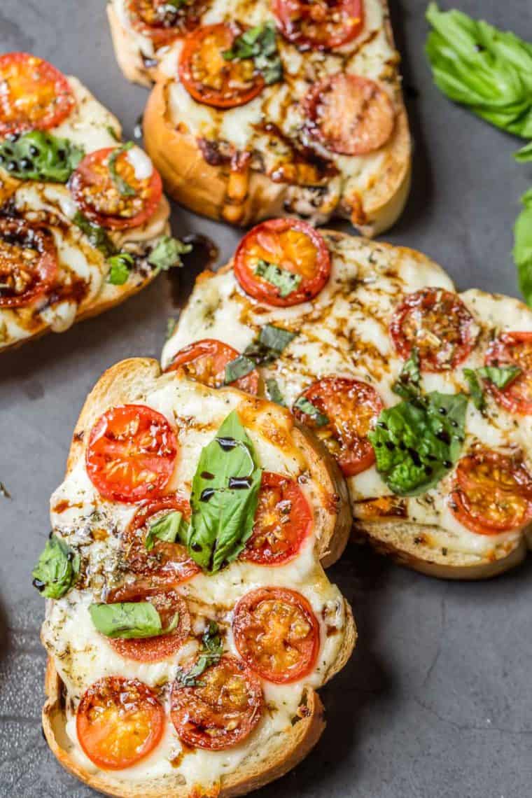 Margherita pizza toast topped with basil and drizzled with balsamic glaze stacked on top of each other. 