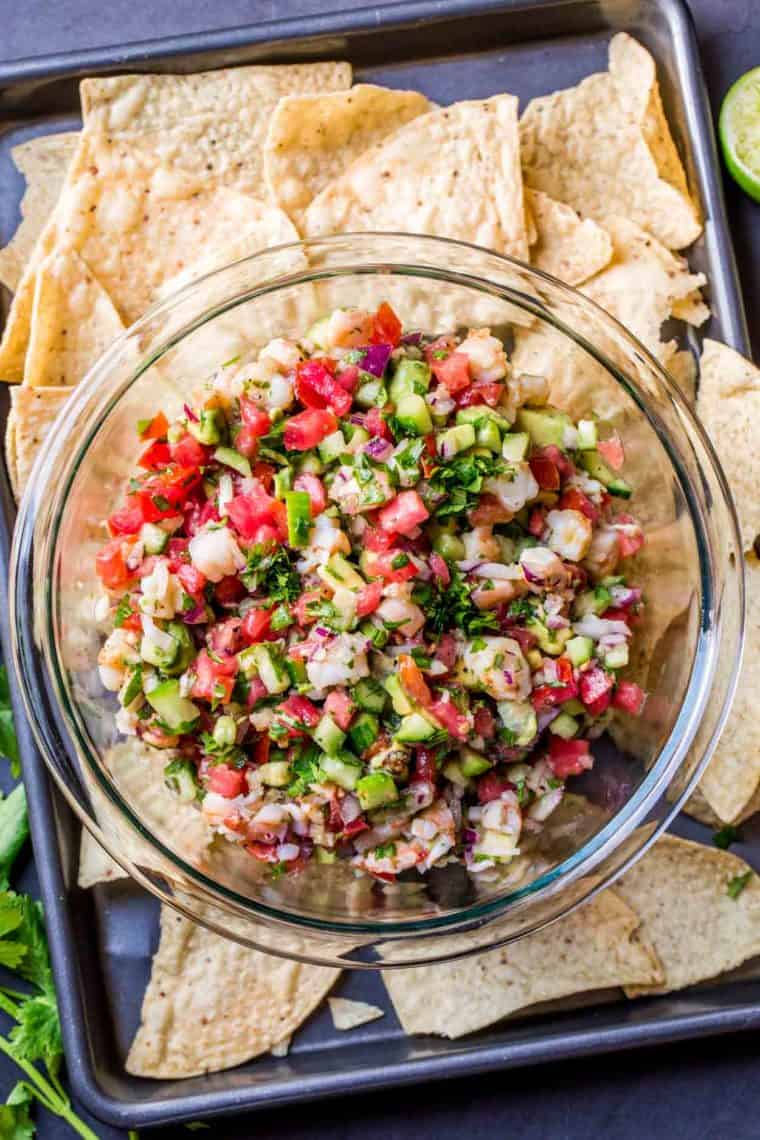 A glass bowl of ceviche topped with fresh chopped greens in a tray with tortilla chips.