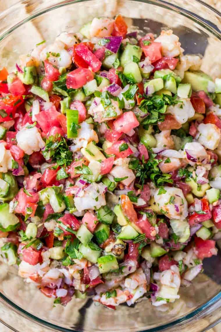 A bowl loaded with with Ceviche loaded with baked shrimp, tomatoes, cucumbers, lime juice and chopped greens. 