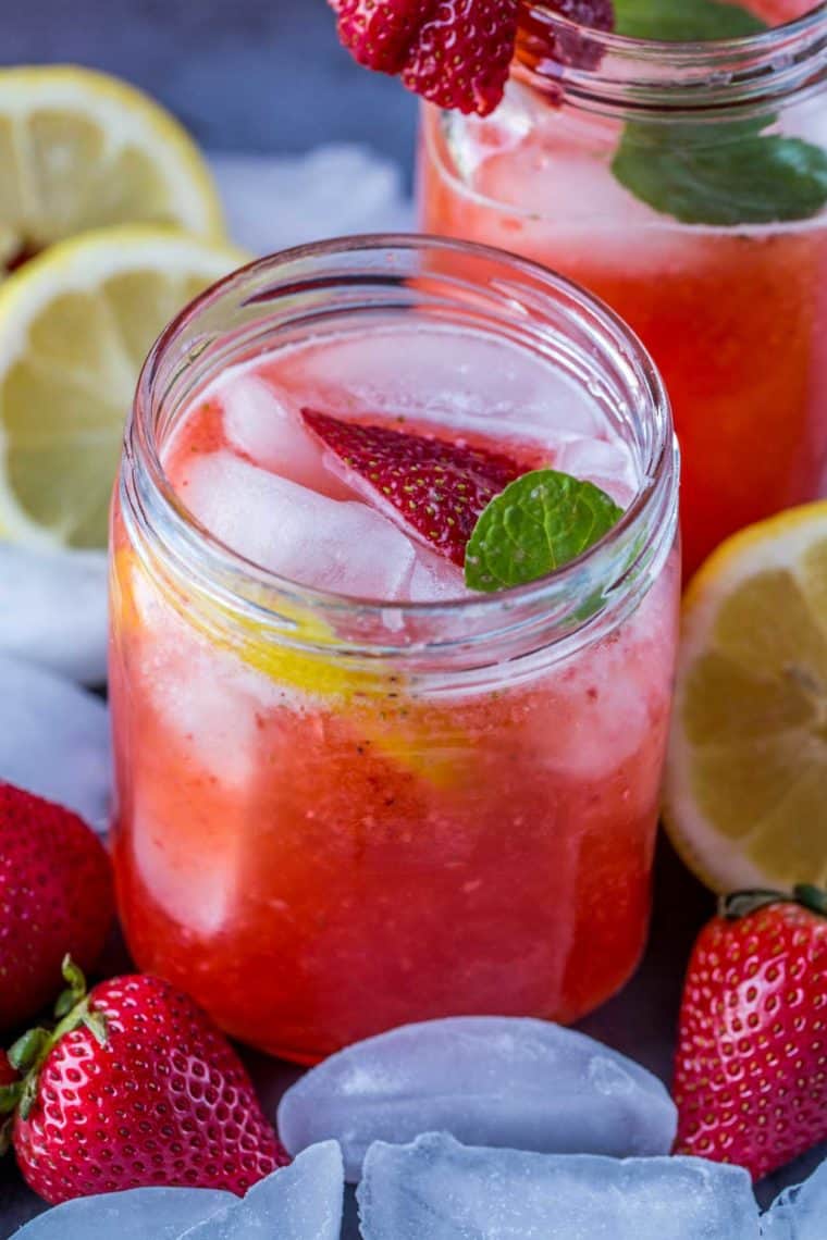 A mason jar filled with Strawberry Lemonade, ice and fresh strawberries with ice cubes and strawberries on the sides.