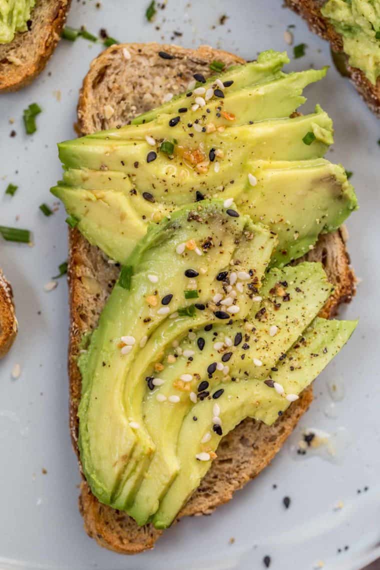 Toasted slice of bread topped with avocado slices drizzled with everything bagel seasoning on a blue plate.