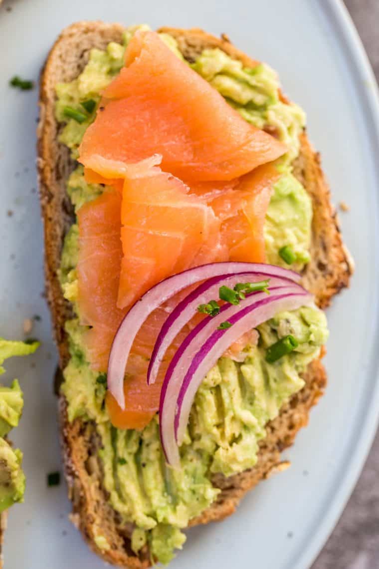 Avocado toast on a blue plate topped with smoked salmon and red onion slices.