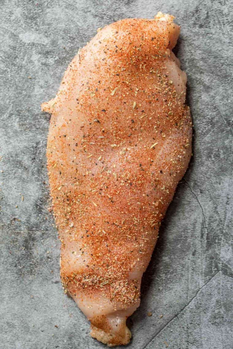 A seasoned chicken breast on a cutting board. 